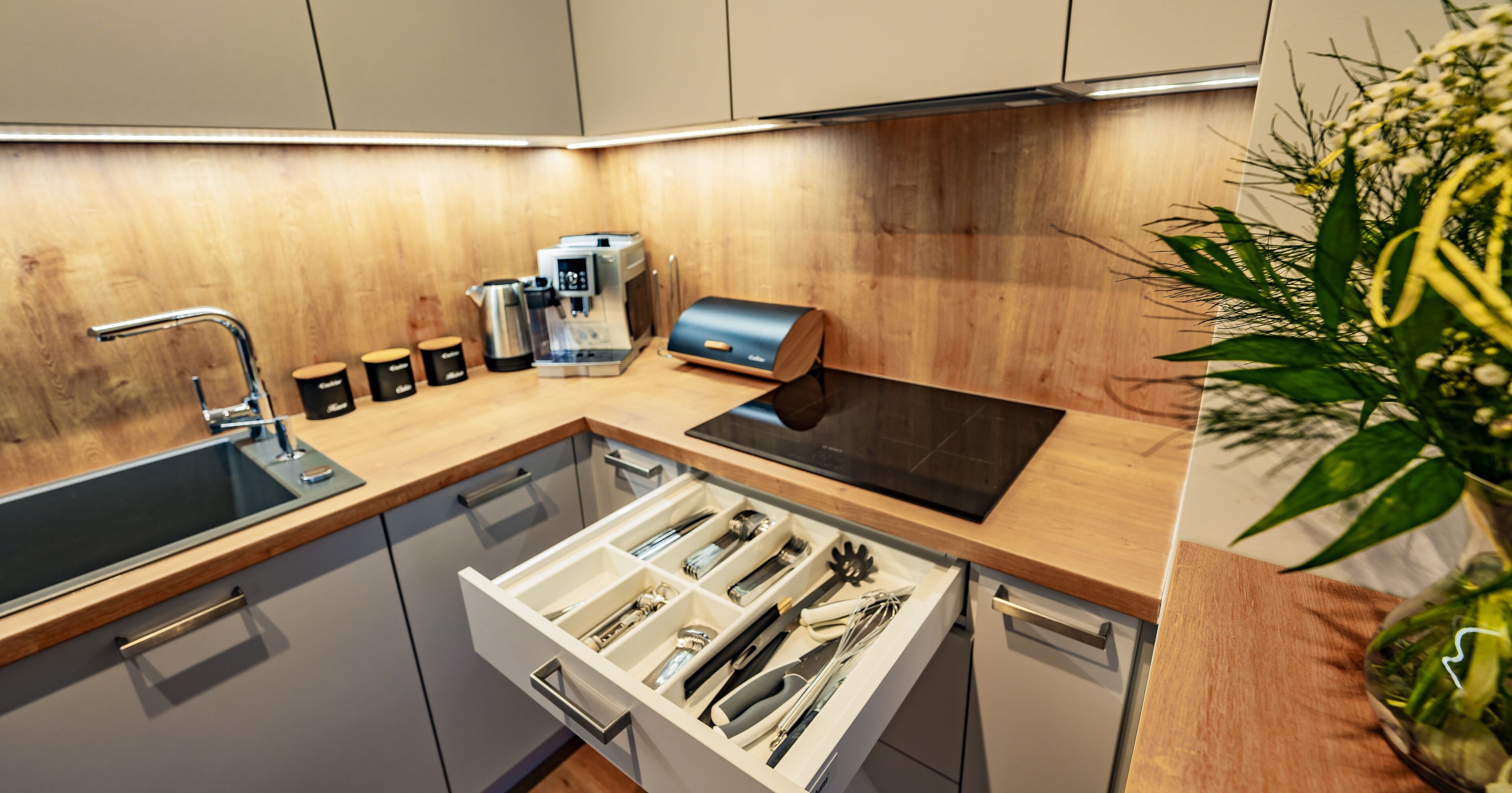A modern kitchen with a built-in dishwasher, a coffee machine, and a variety of utensils in a drawer.