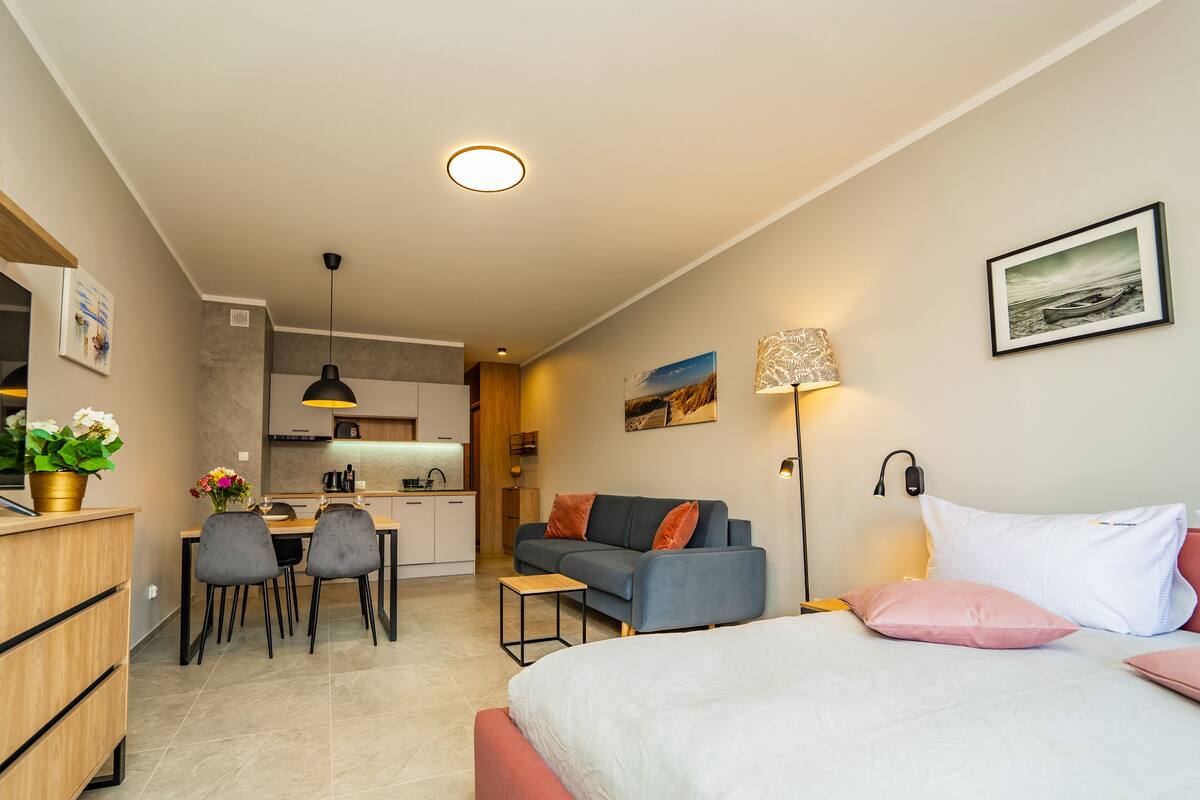 Una habitación moderna y bien iluminada con cama, sofá, comedor y cocina.