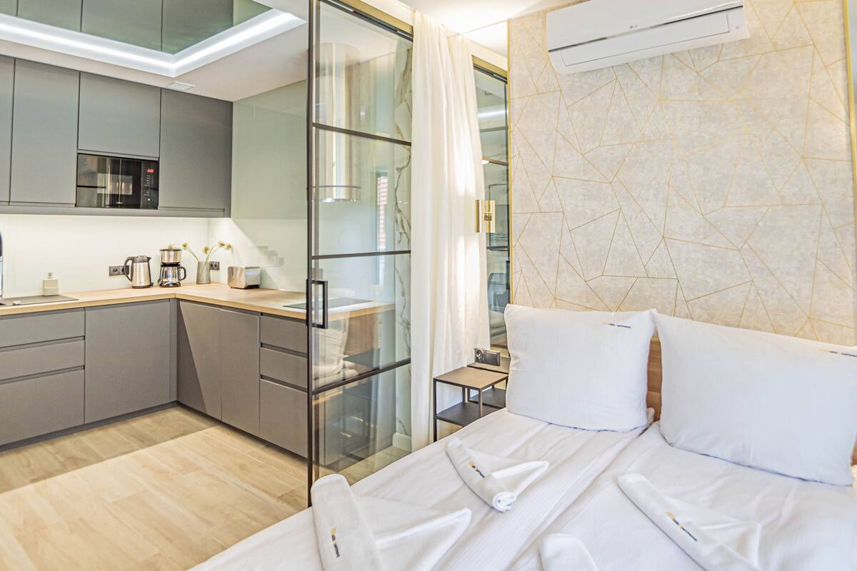 Una habitación de hotel moderna con kitchenette, una cama con ropa blanca y una pared con diseño de mármol.