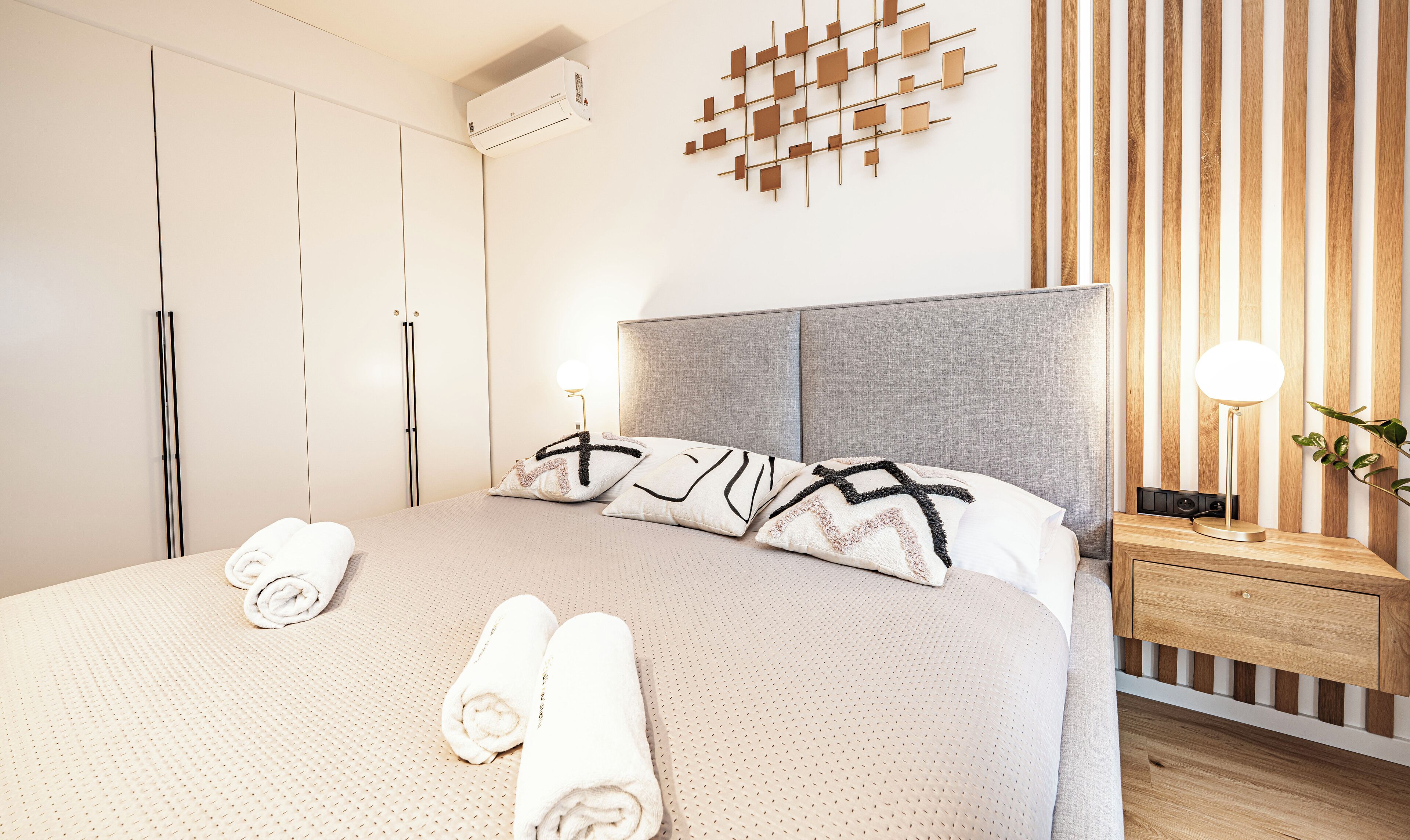 A modern bedroom with a large bed, a grey headboard, and a wooden wall panel.