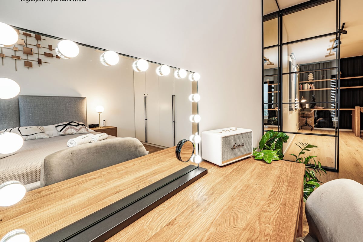 Un dormitorio moderno con cama, mesita de noche, lámpara y espejo con luces.