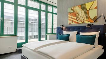 A hotel room with a large bed, a headboard, a painting on the wall, and a window with blinds.