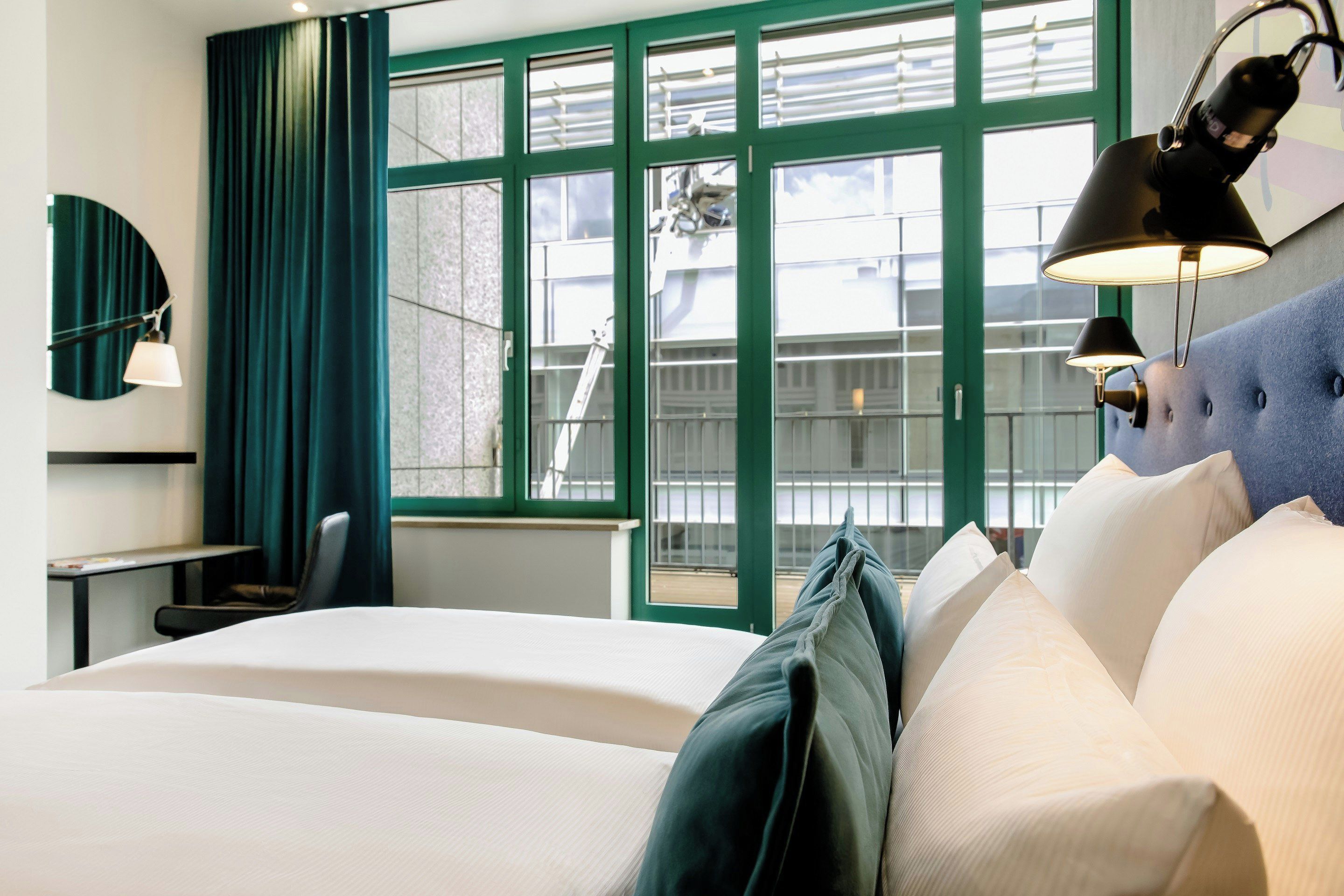 Una habitación de hotel con cama, escritorio, silla y un ventanal con vistas al exterior.
