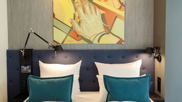 Habitación de hotel con cama, almohadas color turquesa, cabecera y un cuadro de una mano.