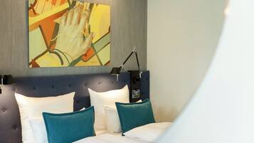 Una cama bien hecha con almohadas blancas y azul verdosas, un cabecero moderno y una obra de arte colgada en la pared.