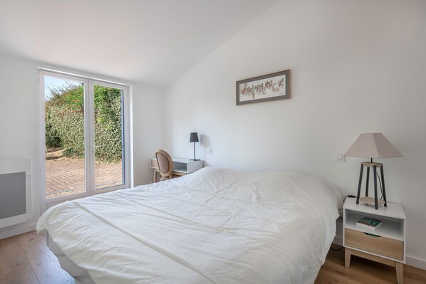 Une chambre à coucher avec un grand lit, un bureau, une chaise, une lampe et une fenêtre donnant sur un paysage verdoyant.