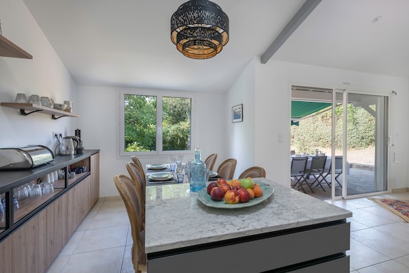 A modern kitchen with a marble countertop, a fruit bowl, and a dining area with chairs.