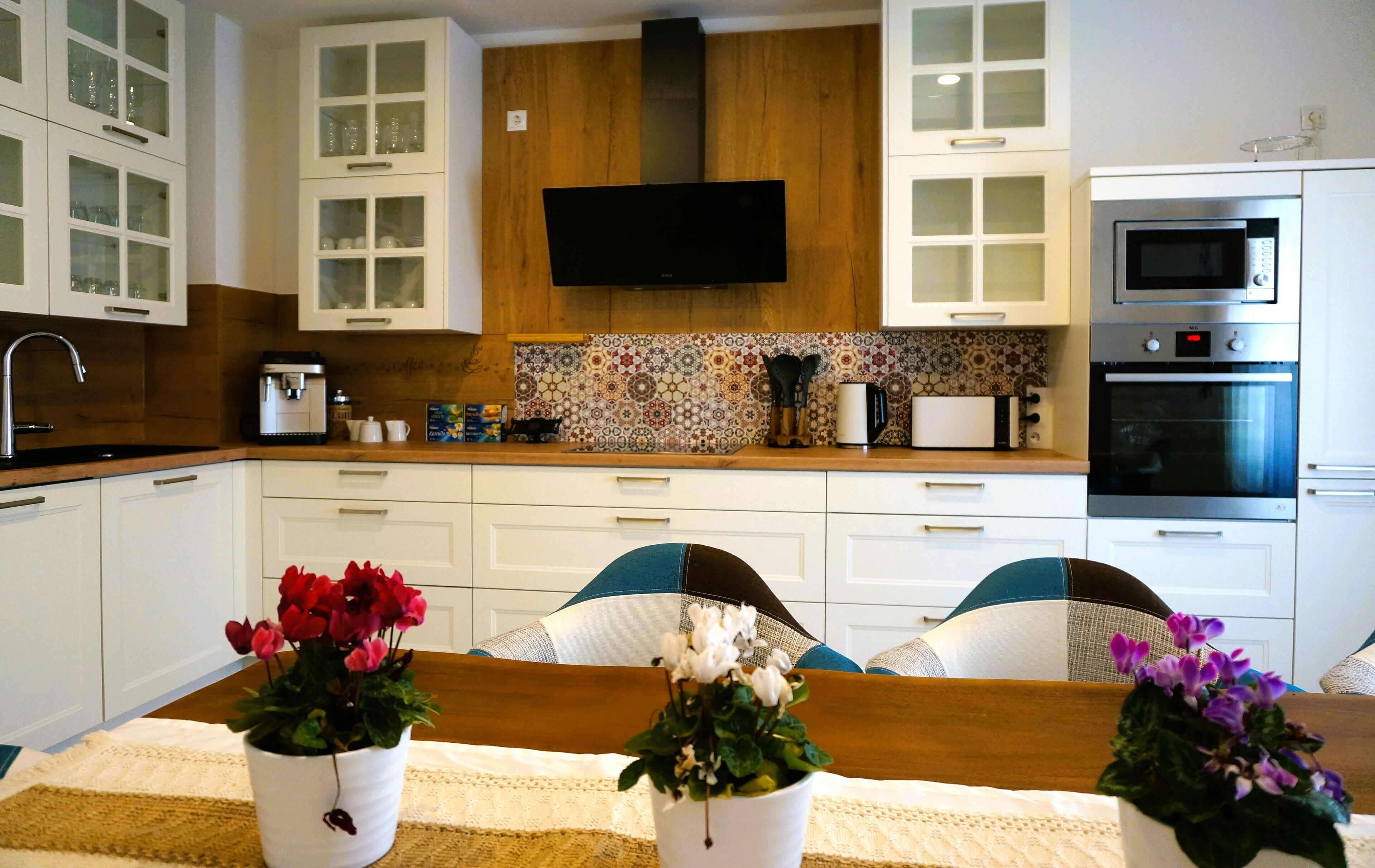 A modern kitchen with white cabinetry, a flat-screen TV, a coffee maker, and a microwave.