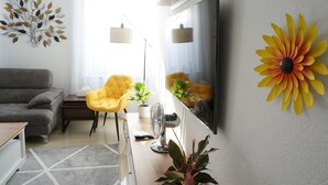 Een moderne woonkamer met een grijze bank, gele fauteuils, een flatscreen televisie en decoratieve muurkunst.