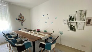 Een eetgedeelte met een houten tafel, blauw-witte stoelen en decoratieve wandkunst, waaronder vlinders en ingelijste foto's.