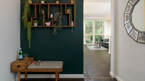Ein Flur mit dunkelgrüner Wand, einer Holzbank und einem an der Wand befestigten Pflanzregal.