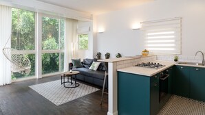 Eine moderne Küche mit Kochinsel, einem Essbereich inklusive Sofa und Tisch, und großen Fenstern mit Blick ins Grüne.