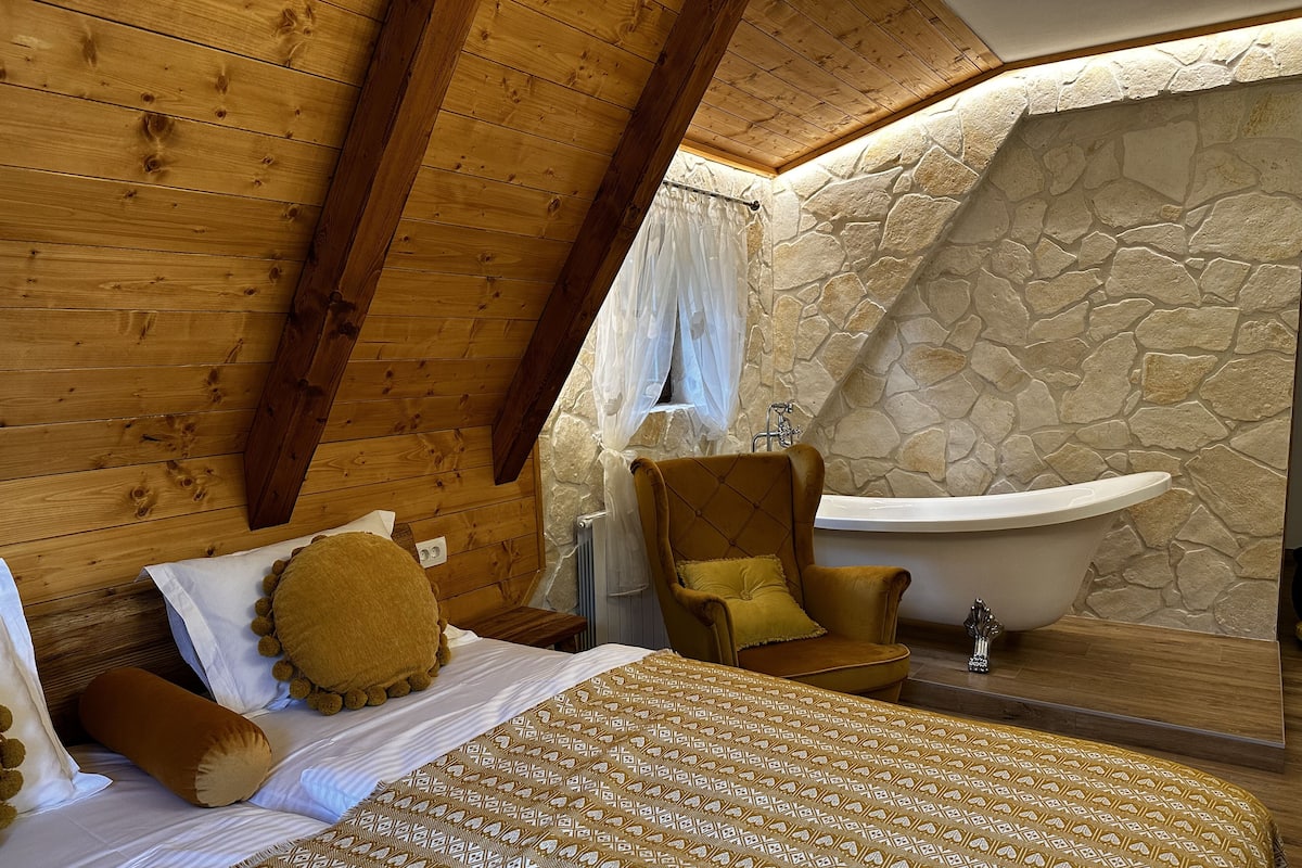 Ein Schlafzimmer mit einem Bett, einem Sessel, einer Steinsäule und einer Badewanne.