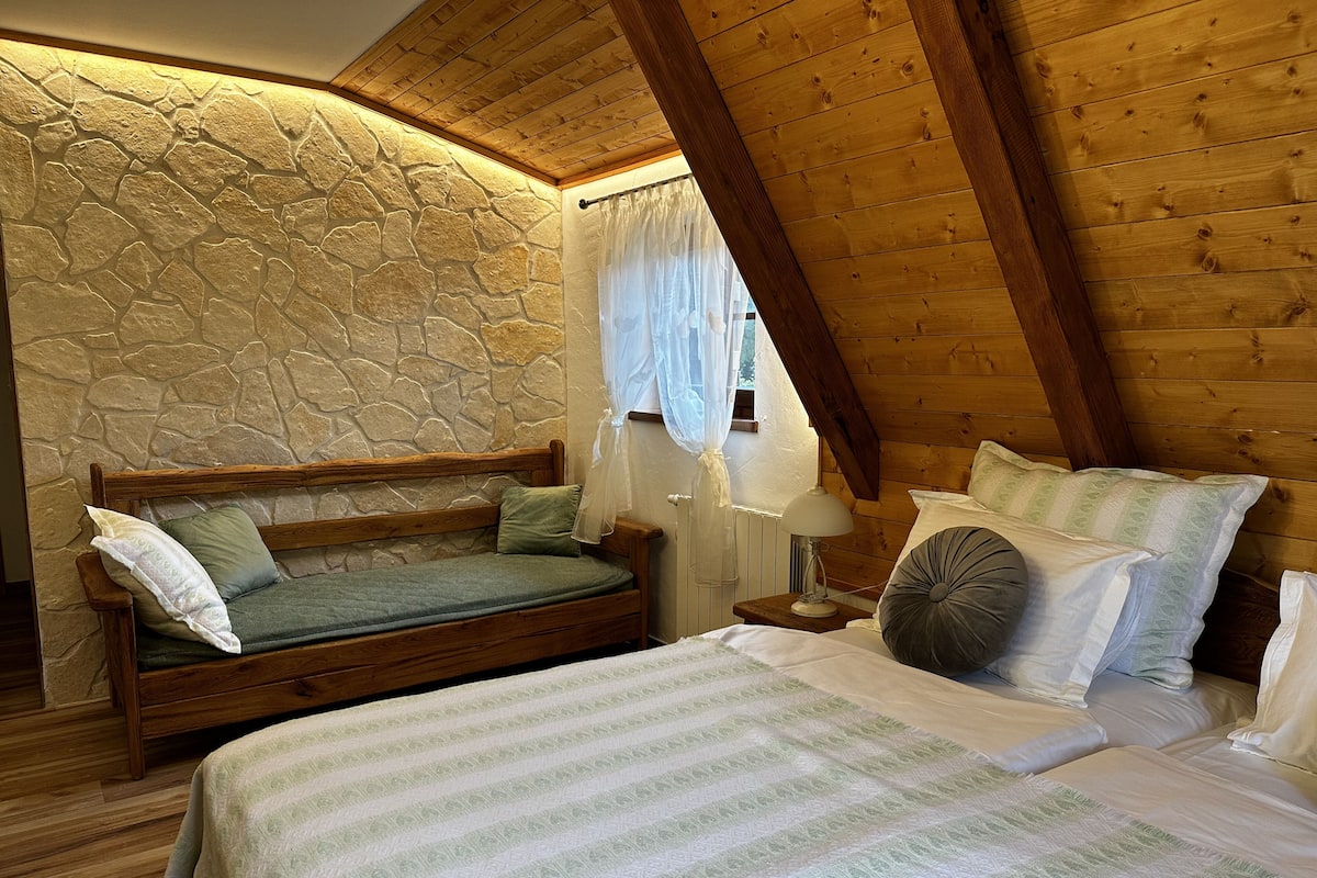 Ein gemütliches Schlafzimmer mit Steinwand, Holzbalken, einem Bett mit gestreifter Bettdecke und einem Nachttisch mit Lampe.