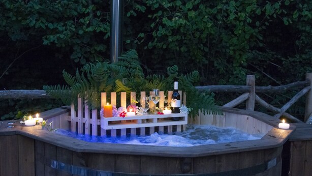Un jacuzzi de madera con valla de madera, velas y flores.