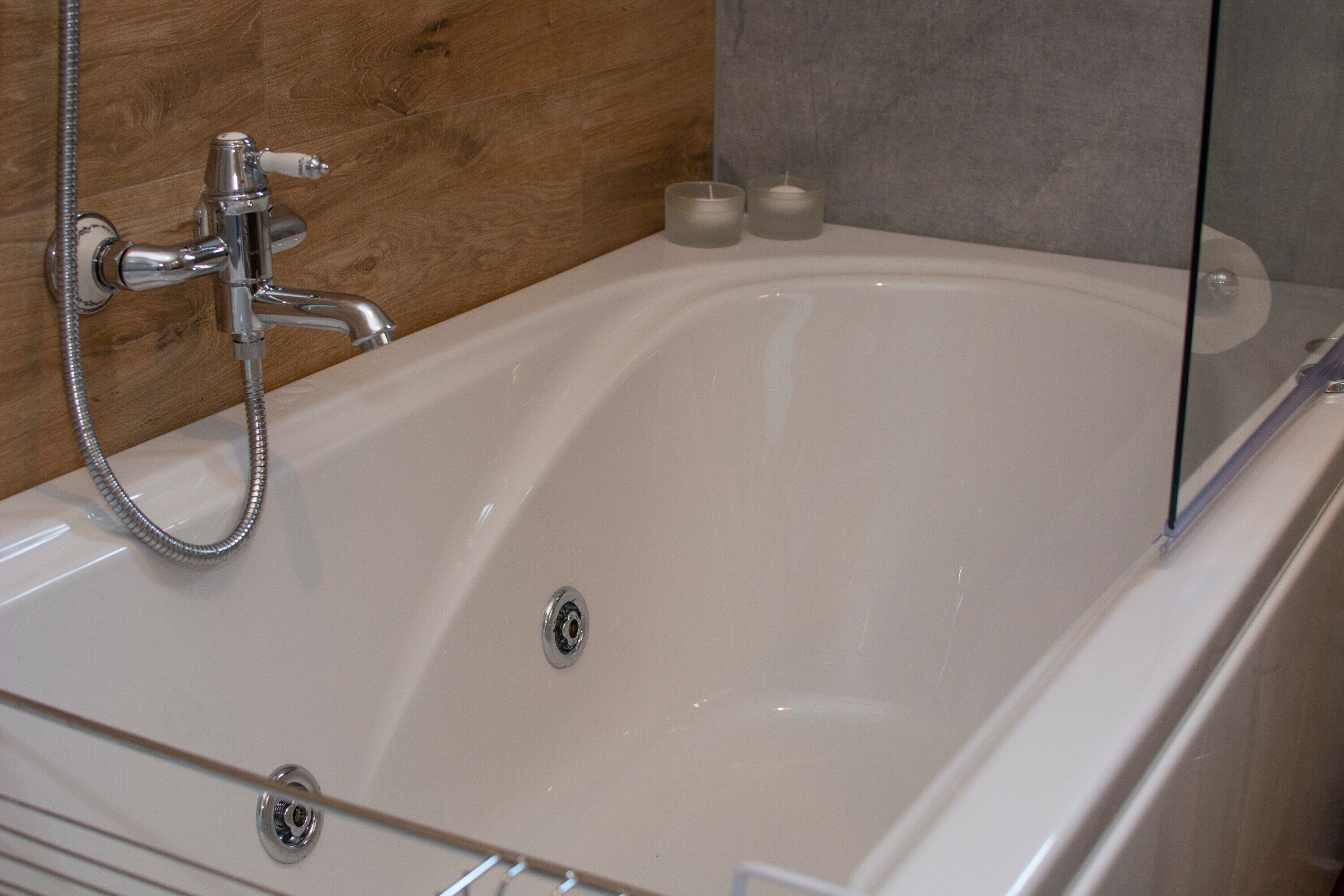 Eine weiße Badewanne mit Duschbrause, zwei Kerzen und einer Glasabtrennung.