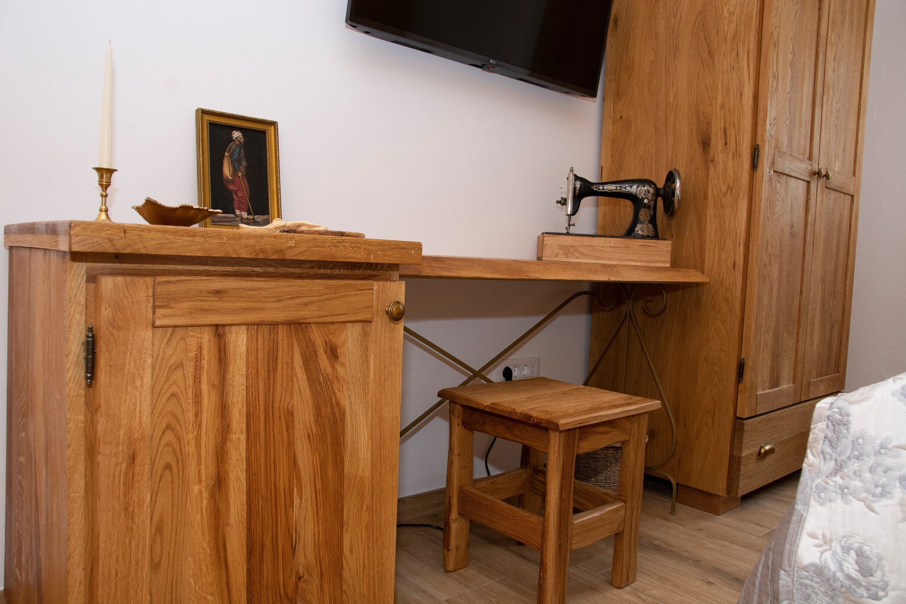 A wooden desk with a sewing machine, a small stool, and a framed picture on the wall.