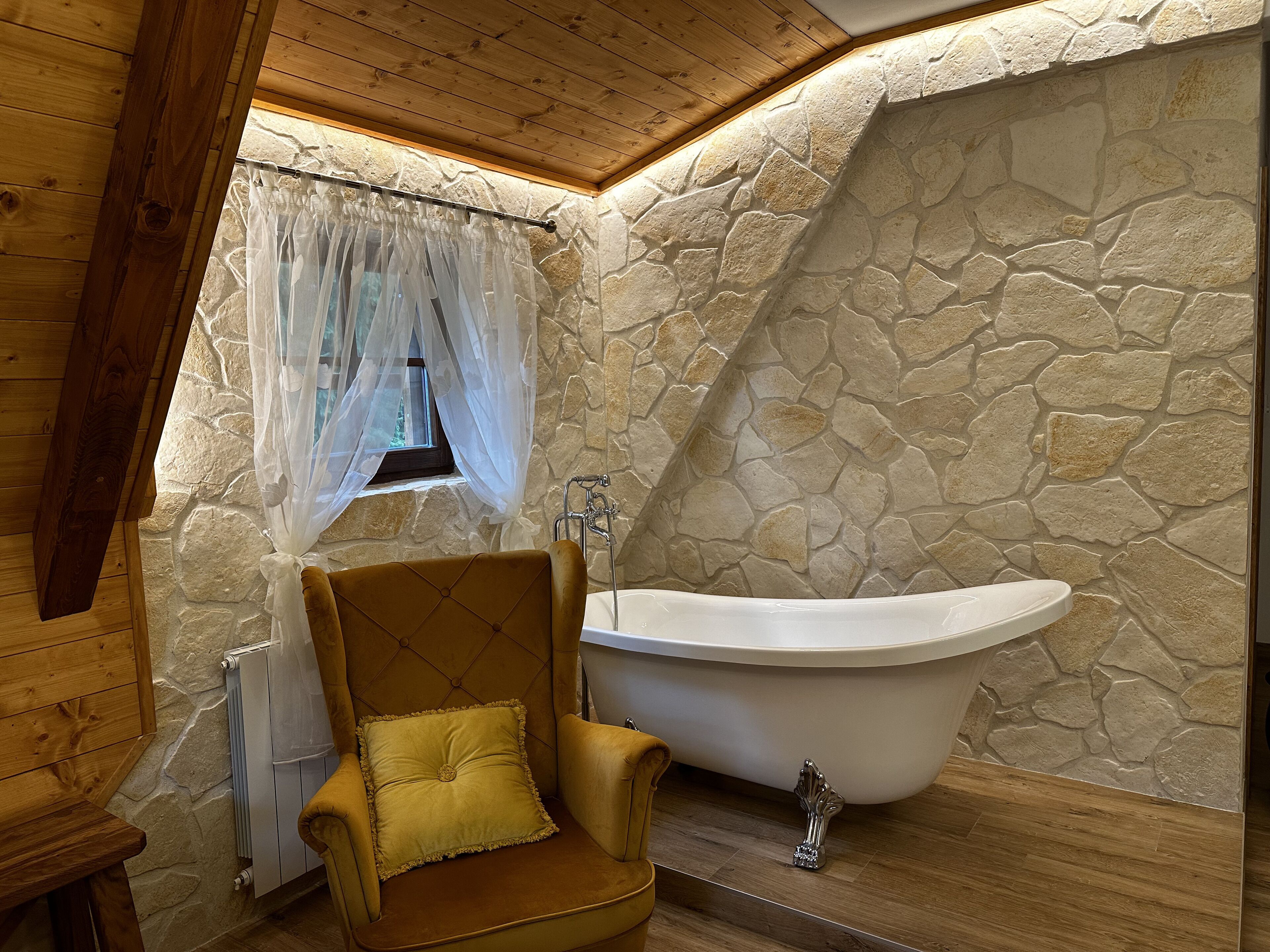 A bathroom with a stone wall, a bathtub, and a wooden chair.