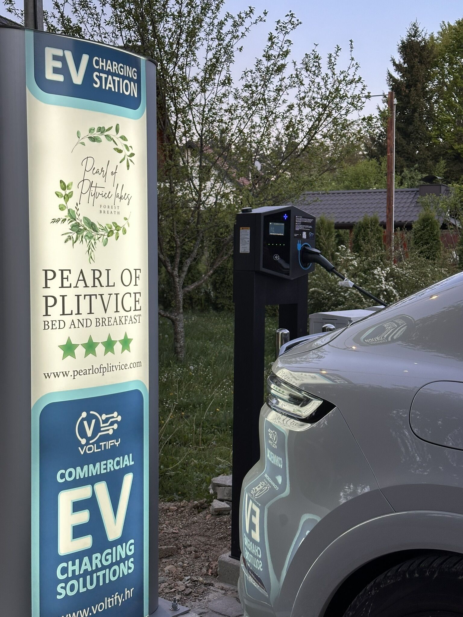 An EV charging station with a sign for 'Pearl of Plitvice Bed and Breakfast' and 'Voltify Commercial EV Charging Solutions'.