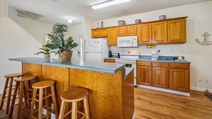 Cozinha com armários de madeira, uma ilha central com banquetas, micro-ondas e geladeira.