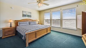 Quarto com cama de madeira, ventilador de teto e três janelas com cortinas.