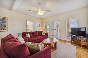 A living room with a red sofa, a wooden coffee table, a ceiling fan, and a TV on a wooden stand.