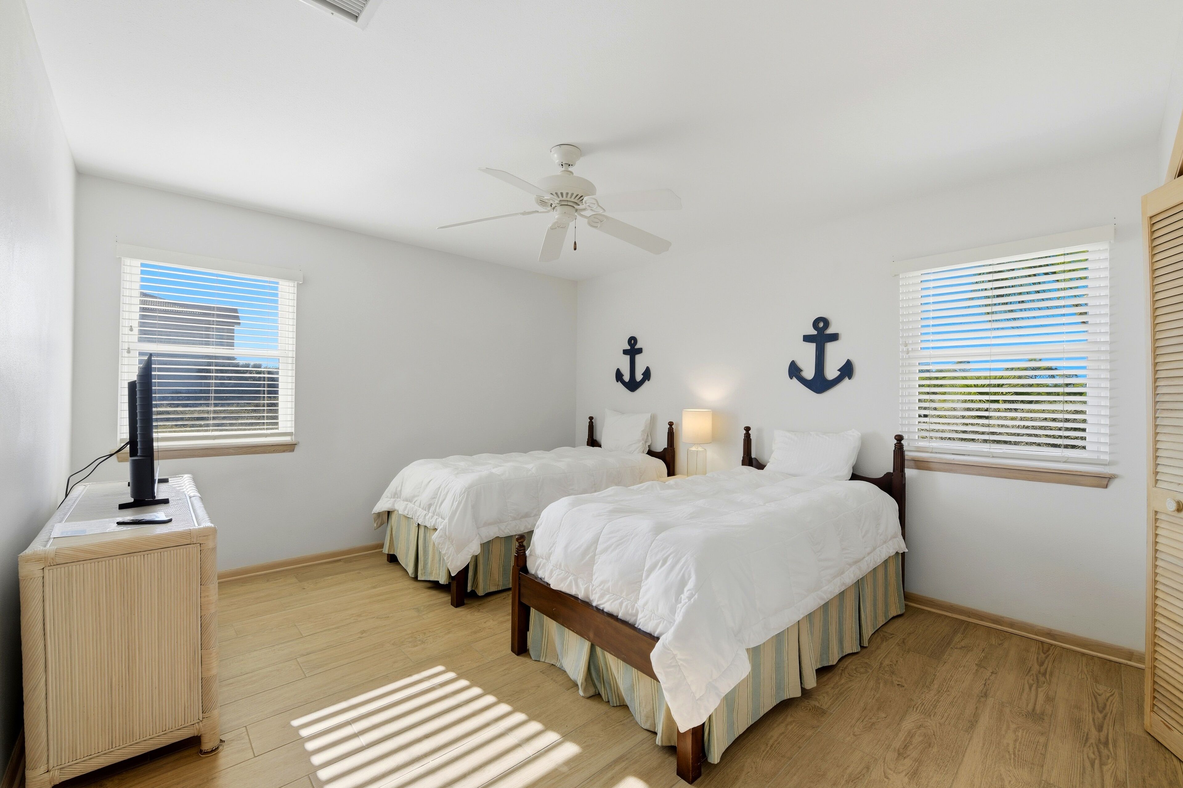 A bedroom with two beds, a ceiling fan, and two windows with blinds.