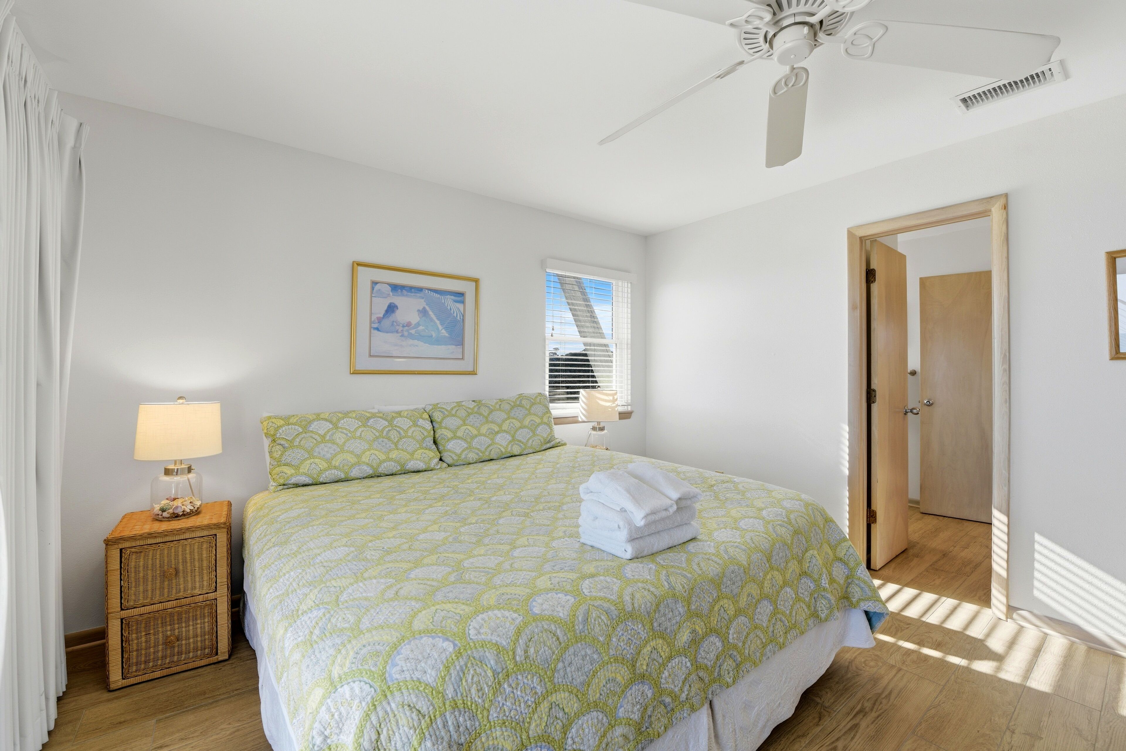 A bedroom with a bed, a nightstand, a ceiling fan, and a window with blinds.
