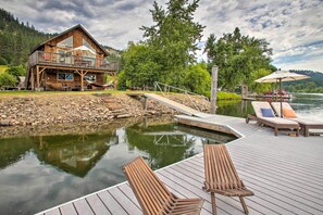 A wooden cabin with a balcony overlooking a lake, a dock with lounge chairs, and a stone pathway leading to the cabin. - Waterfront Cabin w/ 2 Boat Docks & Mtn Views! (St Maries)