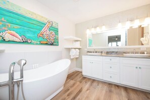 Une salle de bain moderne avec une baignoire sur pieds, un grand miroir et un plancher en bois.