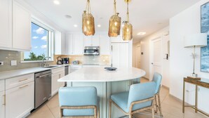 A modern kitchen with white cabinets, a central island with bar stools, stainless steel appliances, and hanging gold pendant lights.