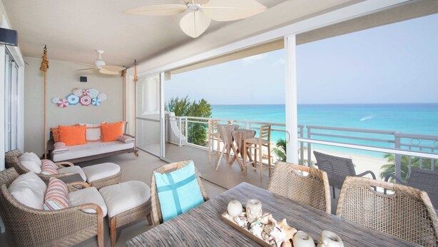 A balcony with wicker furniture, a wooden table, and a view of the ocean.