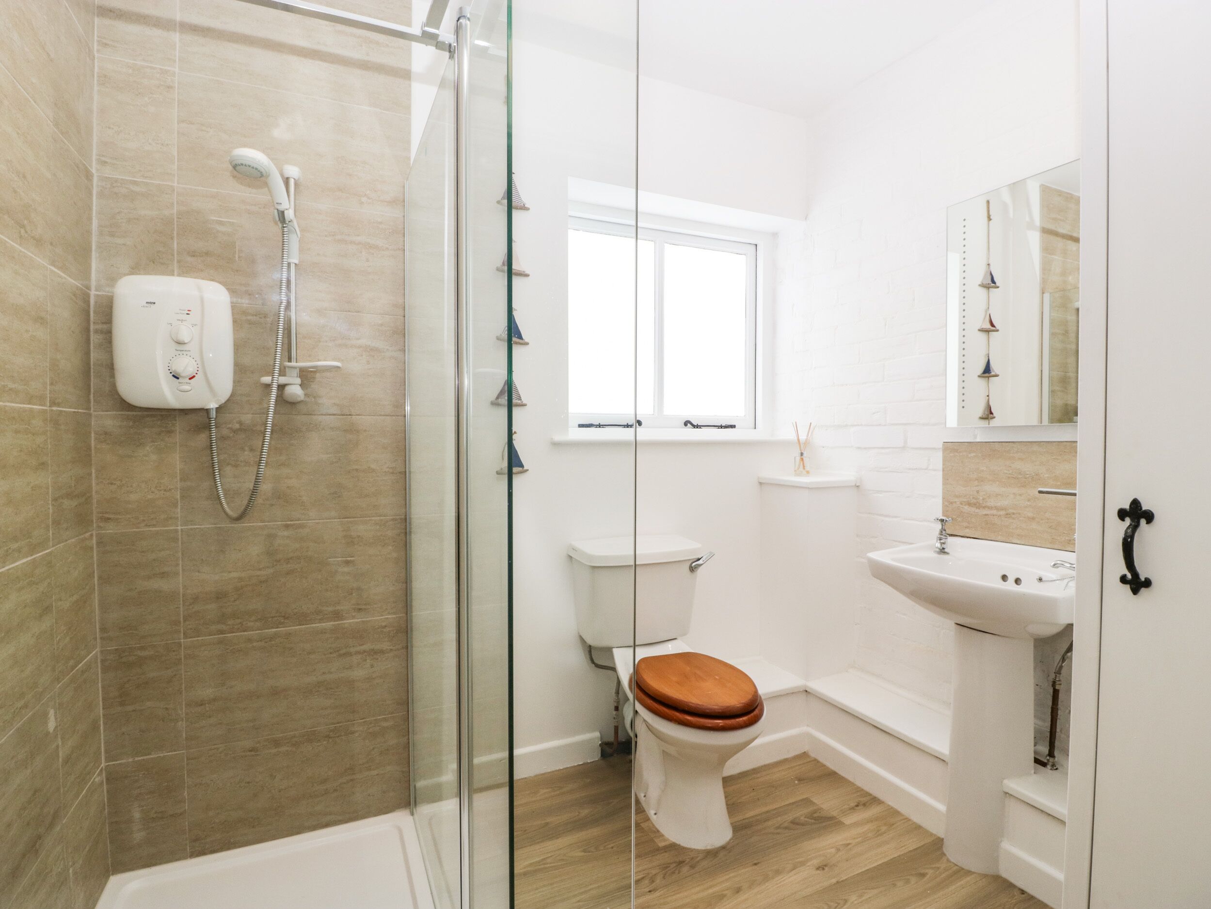 Une salle de bain moderne avec une douche à parois de verre, des toilettes avec un abattant en bois et un lavabo blanc avec un miroir au-dessus.
