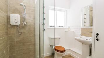 Une salle de bain moderne avec une douche à parois de verre, des toilettes avec un abattant en bois et un lavabo blanc avec un miroir au-dessus.