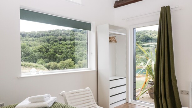 Ein Schlafzimmer mit Bett, Stuhl, Kleiderschrank und Fenster mit Blick auf einen Wald.