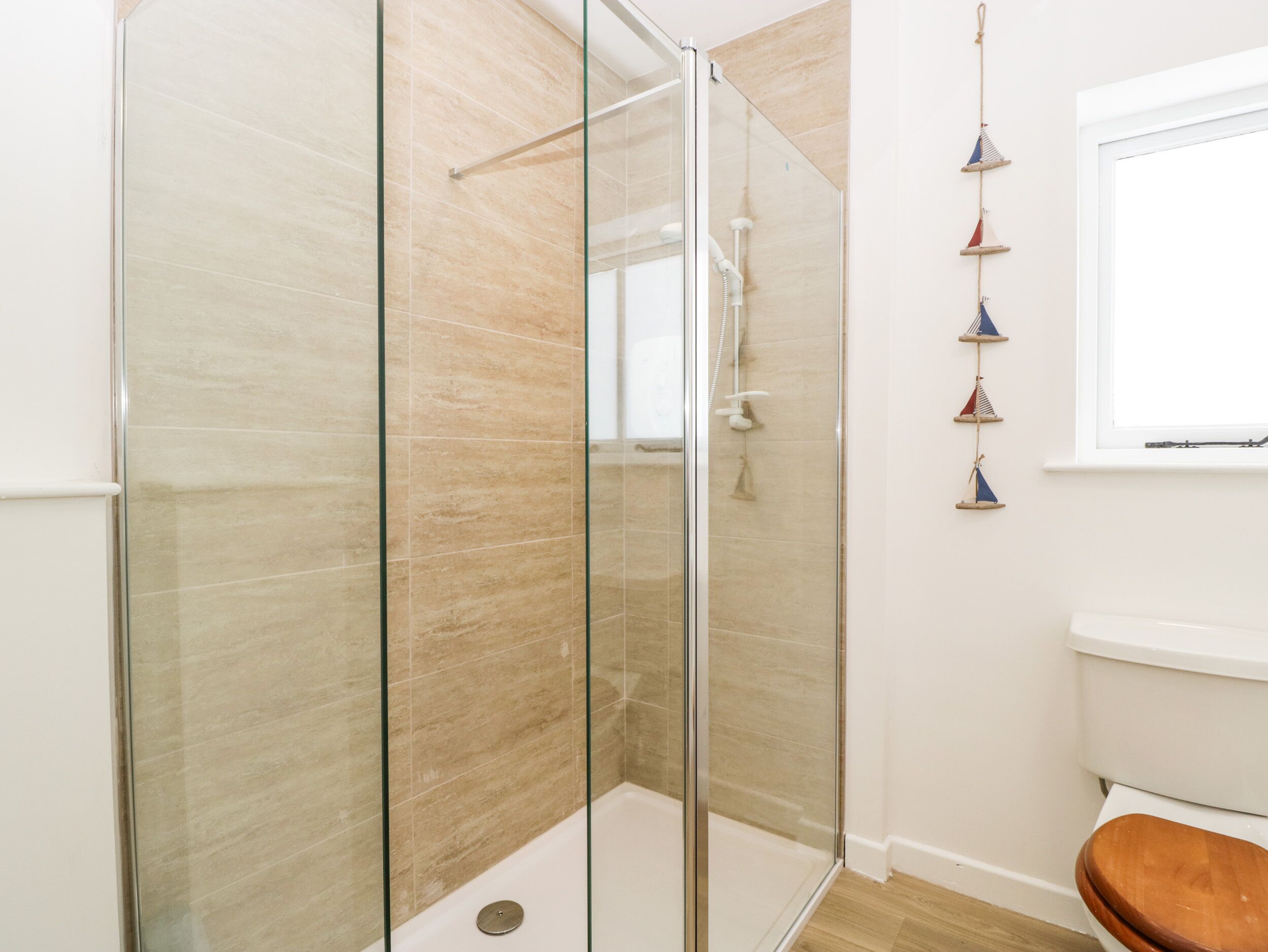 A modern bathroom with a glass shower enclosure, a toilet, and a wooden bath seat.