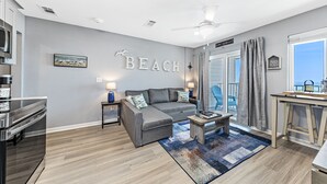 A modern living room with a gray sofa, a coffee table, and a view of the ocean through large windows. - Plantation 4514 (Gulf Shores)
