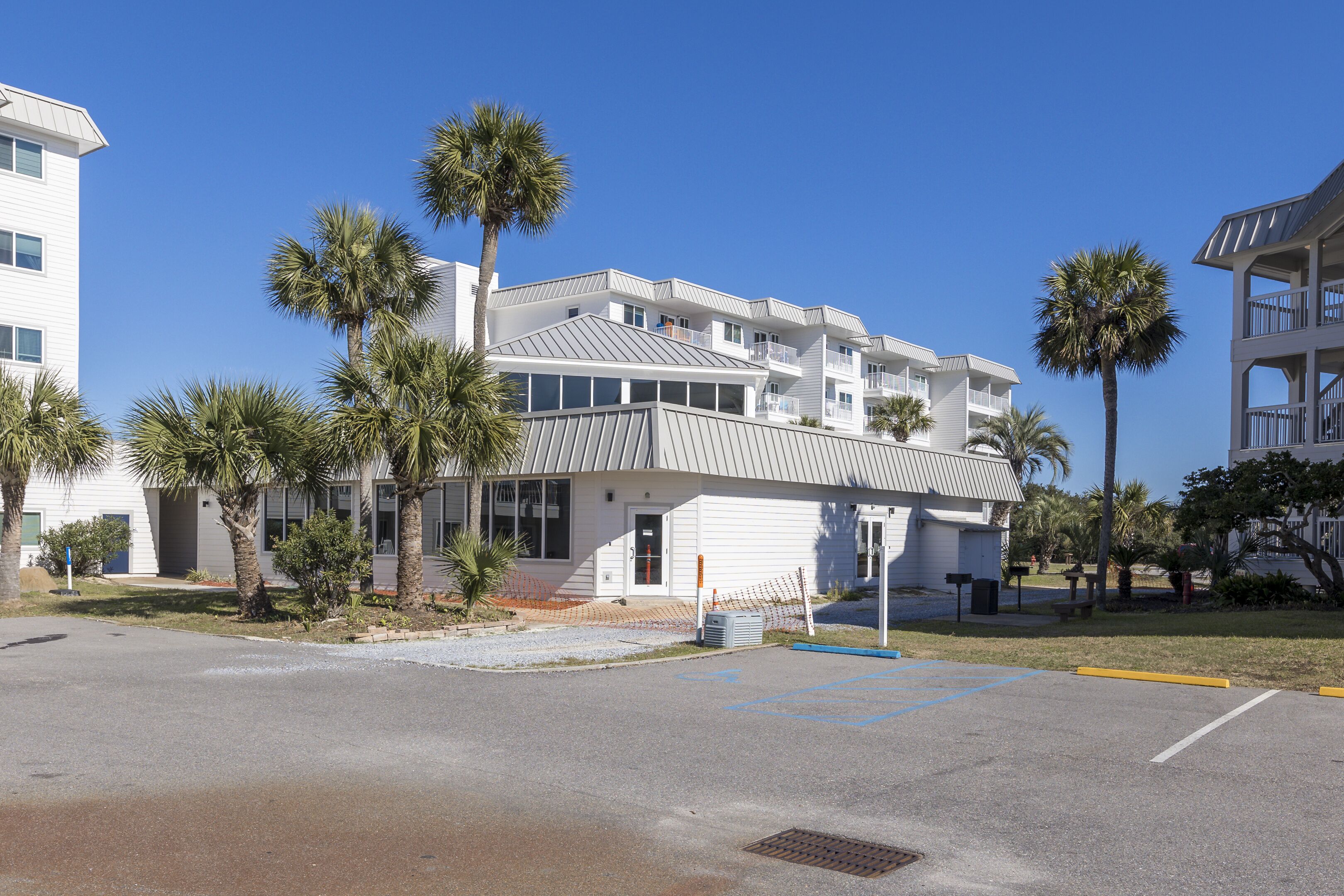 A multi-story hotel with a flat roof, white exterior, and balconies. There are palm trees in front of the building.
