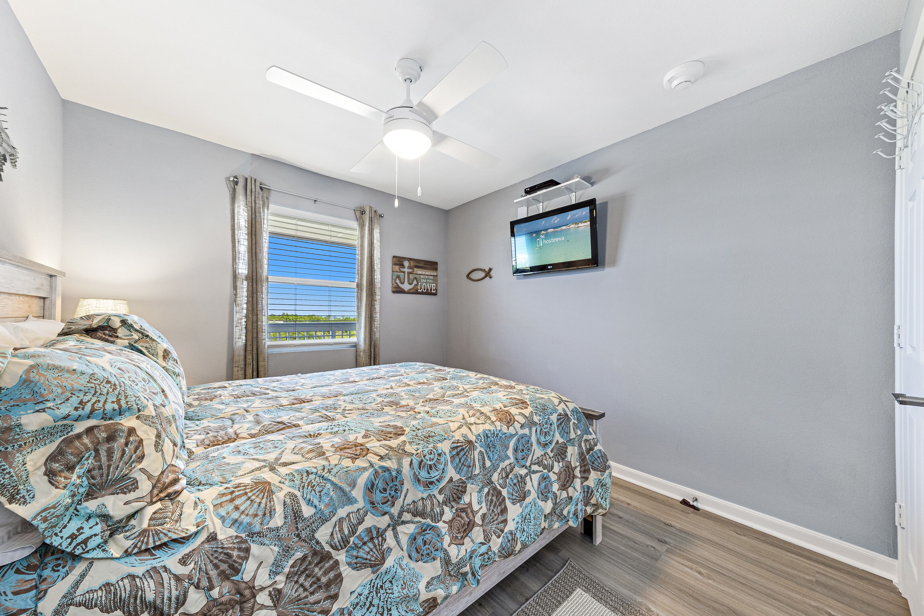 A bedroom with a bed, a ceiling fan, a TV, and a window with curtains.