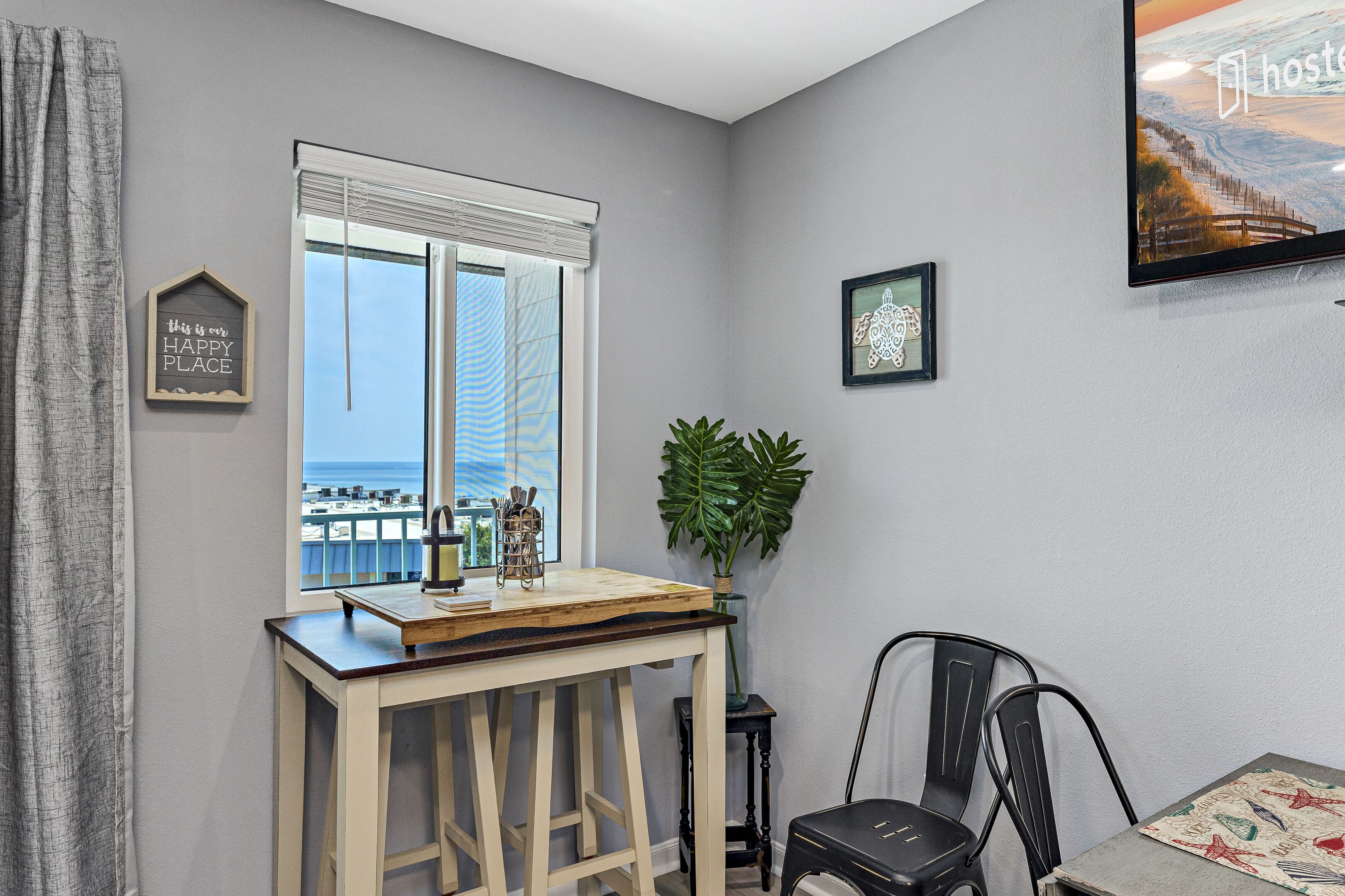 A room with a view of the ocean, a wooden table with a plant, and a framed picture on the wall.