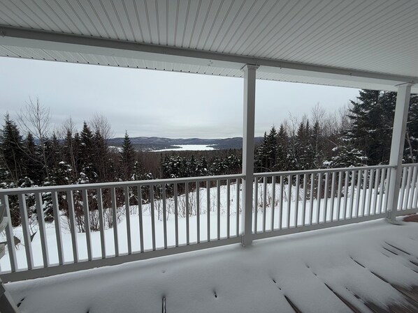A snow-covered deck with a view of a lake and forest.