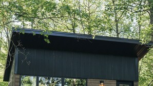 Una cabaña moderna con fachada de madera, una terraza de madera y una escalera que lleva a un balcón.