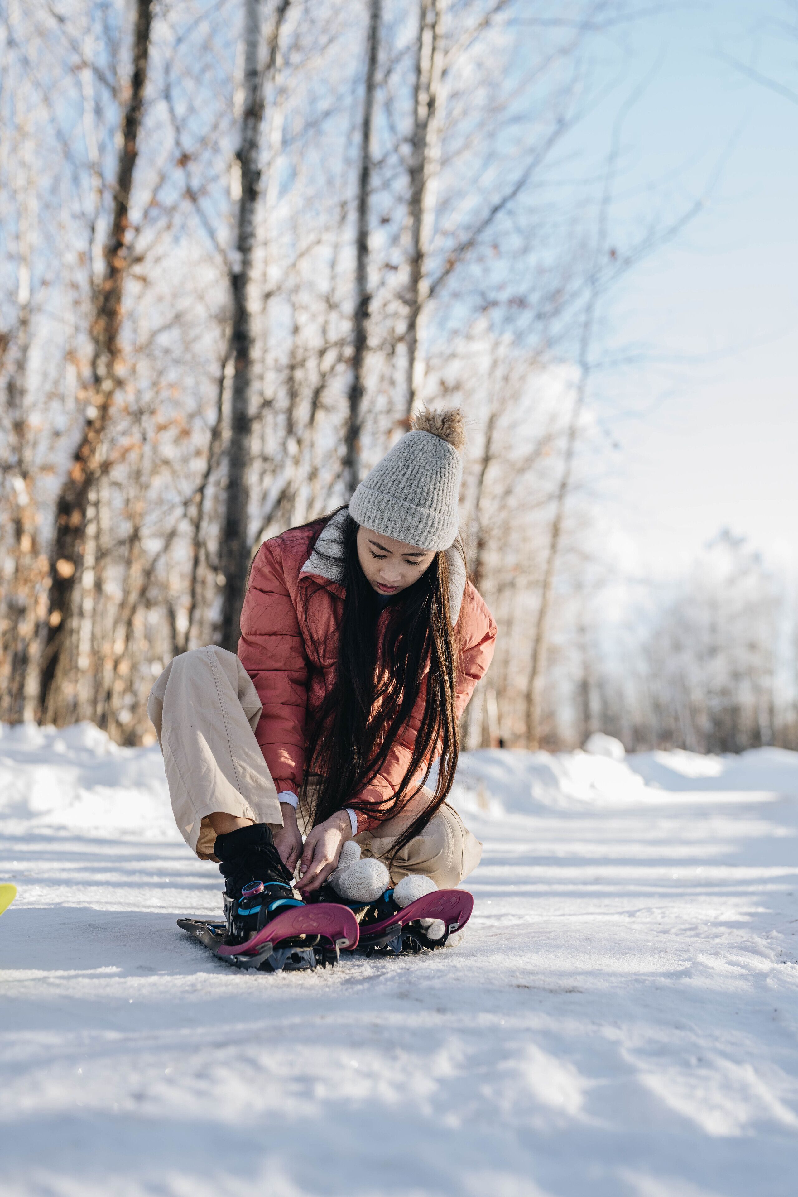 A person sitting on the snow, tying their boots.