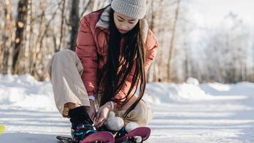 A person sitting on the snow, tying their boots.