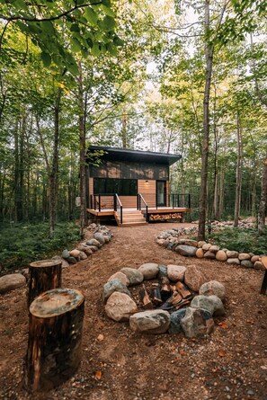 Eine Hütte im Wald mit Feuerstelle und Terrasse.