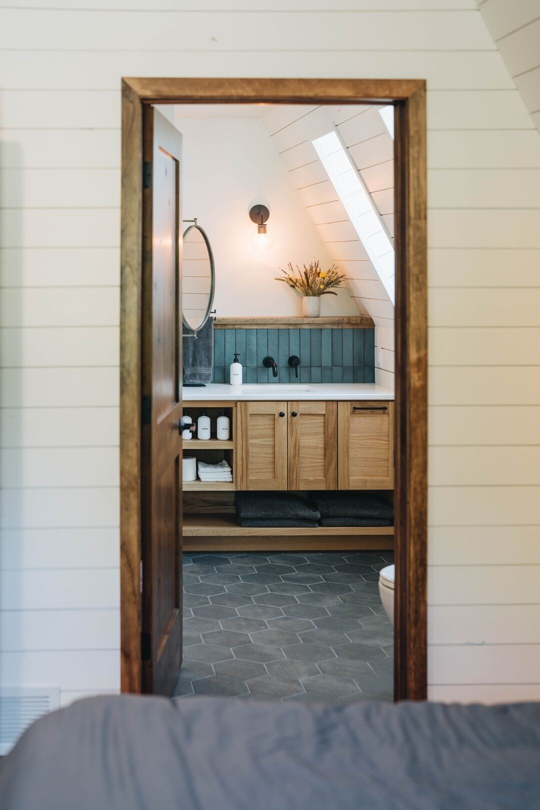 Una habitación con puerta de madera, un baño con pared de azulejos azules, un lavabo y un perchero para toallas.