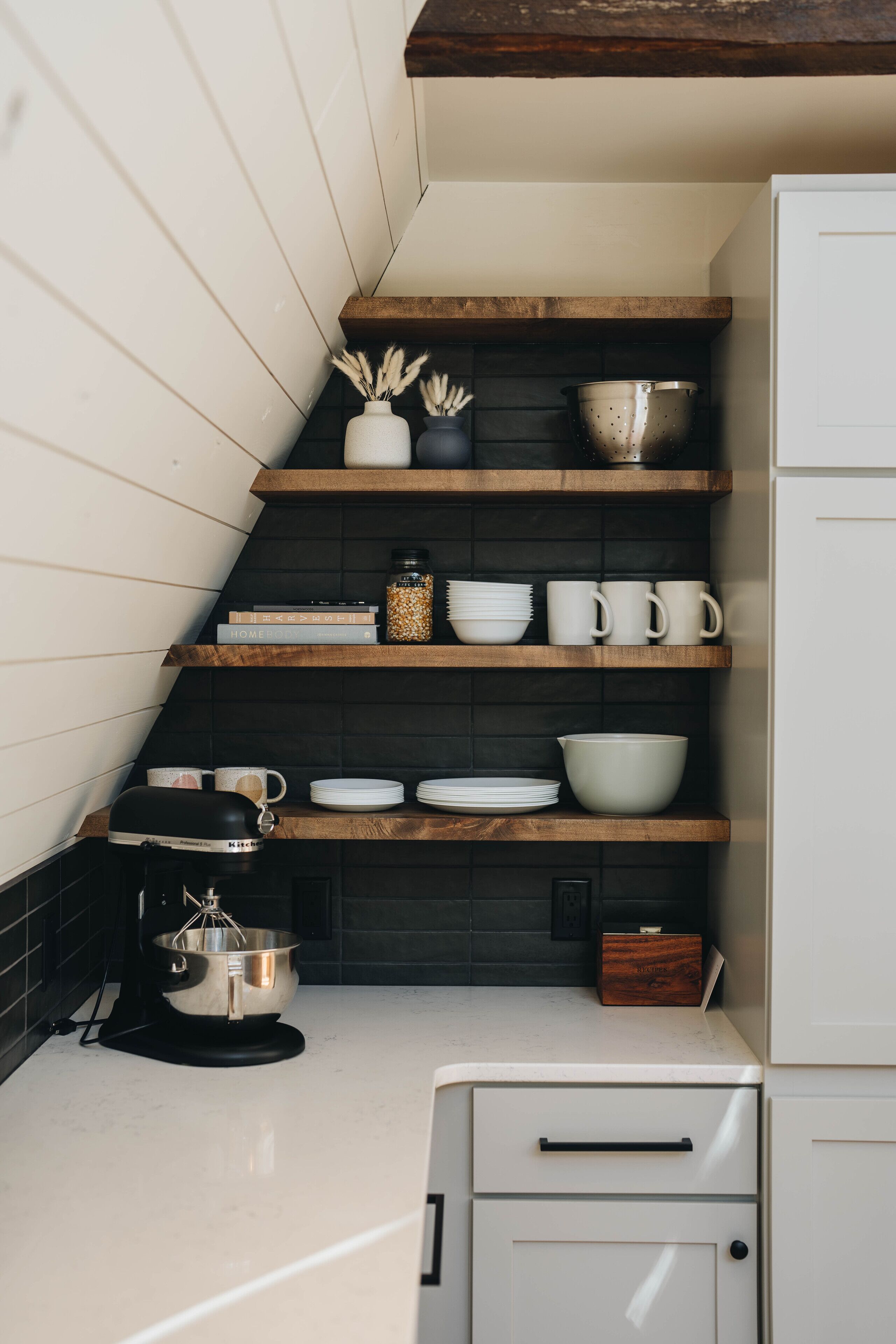 A kitchen with wooden shelves, white cabinets, and a black backsplash.