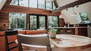 A modern kitchen with large windows, a round wooden table, and a seating area with a plant.