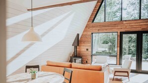 A modern loft with a high ceiling, wooden walls, a large window, and a cozy seating area.