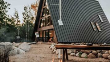 Een modern gebouw met een schuin dak, een vuurkorf met houtblokken en een houten terras.
